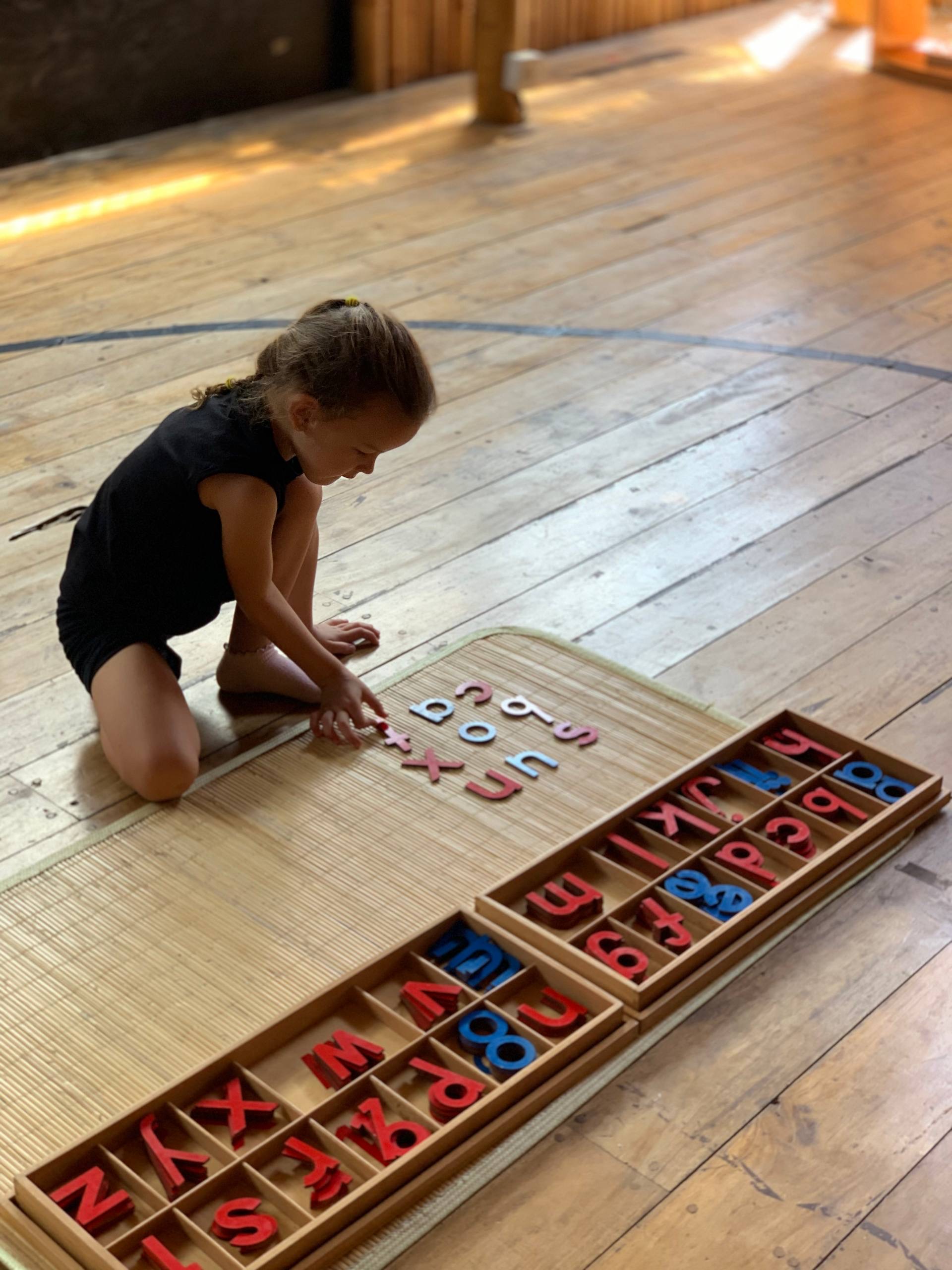 A child arranging the Montessori movable alphabet on the floor at Balu Kids
